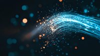 Glowing blue fiber optic strands with orange light particles against dark background create dynamic motion effect for technology and communication concepts.