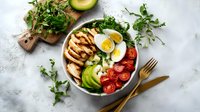 Healthy protein bowl with grilled chicken, avocado, boiled egg, cherry tomatoes and fresh herbs on light background.
