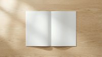 Open blank white book or magazine spread on wooden table surface with natural lighting and shadows for mockup presentations and design projects.