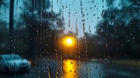 Moody evening scene through rain-covered window with glowing street lamp reflecting on wet surface, creating atmospheric bokeh effect and water droplet patterns.