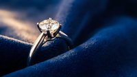 Elegant solitaire diamond engagement ring on luxurious dark blue velvet fabric, sparkling gemstone in silver prong setting, romantic proposal concept.