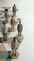 Diverse group of men in beige casual wear standing on geometric hexagonal platforms with modern triangular pattern floor for fashion and lifestyle concepts.