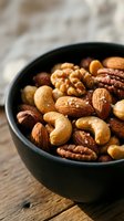 Mixed nuts assortment in dark bowl on wooden table featuring almonds cashews walnuts pecans for healthy snacking and cooking ingredients.