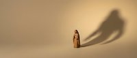 Young woman with long brown hair wearing a beige dress standing against neutral background with dramatic shadow cast on wall behind her, suitable for conceptual and editorial design projects.