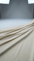 Cream-colored fabric with elegant folds and drapes against neutral studio backdrop, suitable for textile, fashion, and interior design projects.