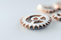 Metallic rose gold gear wheel mechanism on light background with selective focus and copy space, representing business innovation and technology.