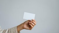 Male hand holding blank white business card against neutral gray background, suitable for corporate branding and marketing materials.