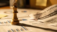 Wooden chess king piece standing on financial newspaper with business charts and graphs, symbolizing strategic business leadership and market analysis.