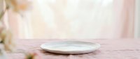 Empty white ceramic plate on soft pink wooden surface with blurred floral background, suitable for food styling, product mockups, and tableware design projects.
