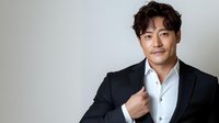 Young Asian male professional in black suit and white shirt against neutral background, confident pose with gentle smile, studio lighting for business portraits.