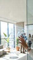 Professional interacting with digital transformation interface on glass panel in modern office environment with natural light and colleagues in background.