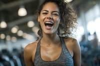 Happy young mixed race woman laughing joyfully in modern gym wearing athletic wear during fitness workout session.