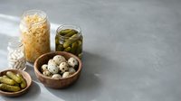 Assorted pickled vegetables and fermented foods in glass jars and wooden bowls on gray surface for healthy eating and food preservation concepts.