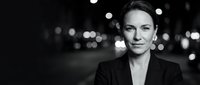 Professional businesswoman in elegant black suit with confident expression against blurred city lights background for corporate and leadership concepts.