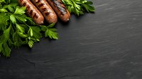 Grilled sausages with fresh parsley leaves on dark slate stone background with copy space for text. Food photography composition.