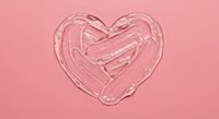 Transparent cosmetic gel smeared in heart shape on pastel pink background, skincare product texture concept for beauty and wellness.