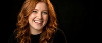 Happy redhead woman with curly hair smiling warmly in black sweater against dark background for lifestyle and portrait photography projects.