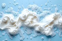 White foam soap bubbles on light blue background with water drops and splashes creating abstract wave pattern for hygiene and cleanliness concept.