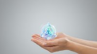 Hands holding glowing water drop with recycling symbol representing environmental protection and sustainability concept on gray background.