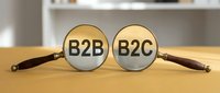 Magnifying glasses revealing B2B and B2C text on wooden table, representing business model comparison and market strategy analysis.