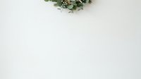 Festive wreath with greenery and berries on white wall, overhead view for holiday greeting cards and seasonal marketing materials.