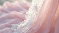 Soft pink chiffon fabric with delicate white lace floral trim, flowing in gentle waves, evoking romance and elegance for fashion and bridal design.