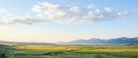 Vast rolling grassland valley with distant snow-capped mountain range under partly cloudy sky, suitable for landscape, travel, and nature editorial use.