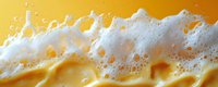 Flowing beer foam and bubbles on golden liquid background in macro photography, showing detailed texture of frothy head and carbonation against amber surface.