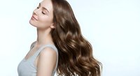 Young woman with long wavy brown hair in gray top against white background. Hair care and beauty concept for salon advertising and cosmetic products.