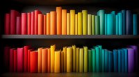 Colorful books arranged in rainbow spectrum order on dark shelves creating vibrant gradient display. Artistic library organization shows spines in red, orange, yellow and blue hues.