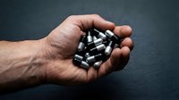 Male hand holding ammunition bullets in palm against dark background, suitable for security, crime, military, and editorial content.