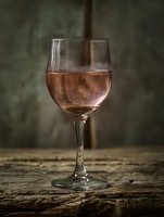 Elegant glass of rosé wine on rustic wooden table with blurred background for restaurant menus, wine tasting events, and culinary marketing materials.