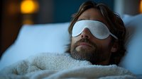 Man with beard wearing sleep mask resting on white pillow in dark bedroom with soft ambient lighting, promoting healthy sleep habits and relaxation.