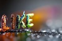Colorful metallic letters spelling LIKE with bokeh background, macro photography showing texture and reflective surface detail for social media concept.