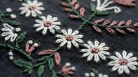 Delicate hand embroidered white daisies with pink centers and green foliage on dark fabric. Traditional needlework craft for textile art and decorative sewing projects.