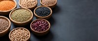 Assorted legumes and pulses in wooden bowls on dark slate surface, including lentils, chickpeas, and beans for cooking and nutrition.