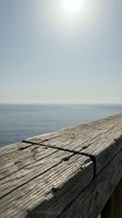 Wooden pier railing with ocean and horizon in soft focus, calm seascape for travel, relaxation, and coastal lifestyle concepts.