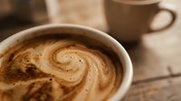 Closeup of latte art with spiral foam design in ceramic cup on wooden surface, coffee shop beverage preparation and serving.