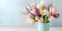 Fresh spring bouquet of pink, purple, and white tulips in mint green vase against soft blue background, perfect for seasonal celebrations.