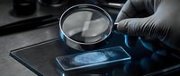 Forensic scientist examining fingerprint evidence with magnifying glass in criminal investigation laboratory for law enforcement analysis.