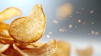 Crispy golden potato chips with salt particles floating in air against blurred background, macro food photography highlighting texture and crunch.