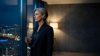 Confident blonde businesswoman in elegant black suit holding whiskey glass by office window overlooking city lights at night for corporate lifestyle.