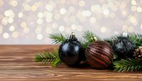 Elegant Christmas ornaments in black and copper with pine branches on wooden table against festive bokeh background.