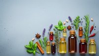 Essential oils in glass bottles with fresh herbs and spices on textured background for aromatherapy and natural wellness products.