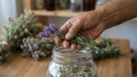 Male hand placing dried lavender flowers into glass jar for herbal storage, preservation, and natural home remedies preparation.