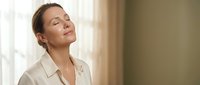 Professional businesswoman with closed eyes enjoying peaceful moment in bright office space for wellness and mindfulness concepts.