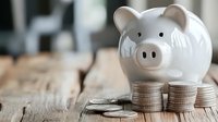 White ceramic piggy bank with stacked coins on rustic wooden table representing savings, financial planning, and money management concepts for budgeting.