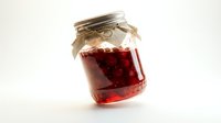 Homemade red fruit jam or preserve in glass mason jar with metal lid and twine, isolated on white background for food packaging and culinary projects.
