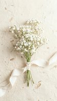 Small bouquet of white baby's breath flowers tied with cream ribbon on textured handmade paper background for wedding invitations and romantic designs.