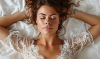 Young Caucasian bride in white lace wedding dress lying on white bedding with closed eyes and peaceful expression, hair spread on pillow, natural makeup look.